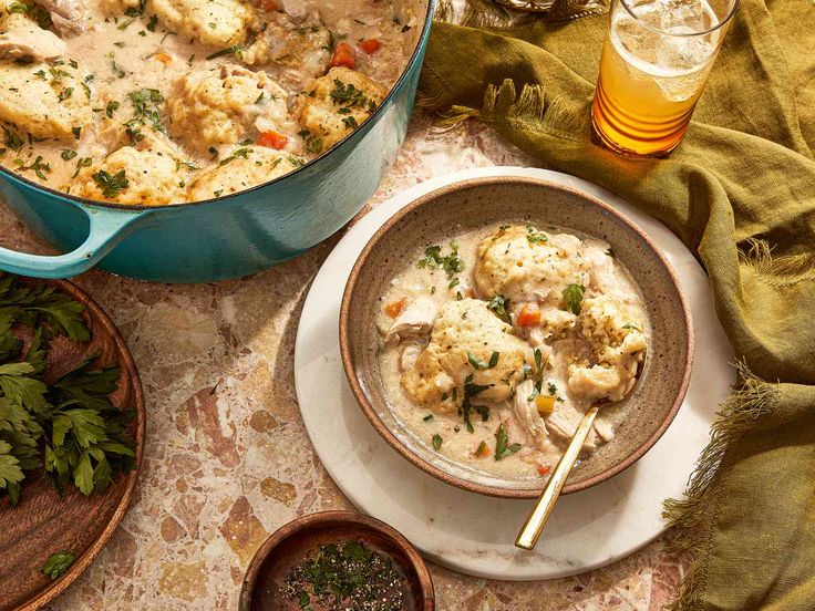 a bowl of chicken and dumpling soup next to a glass of beer