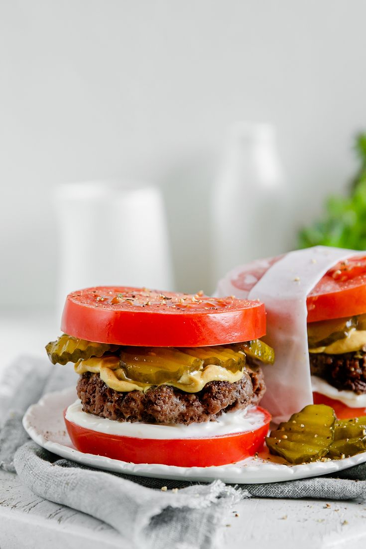 two hamburgers with pickles and tomatoes on a plate