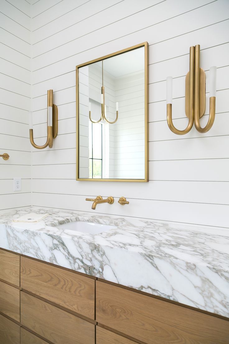 a bathroom with marble counter tops and gold fixtures on the wall, along with two brass sconces