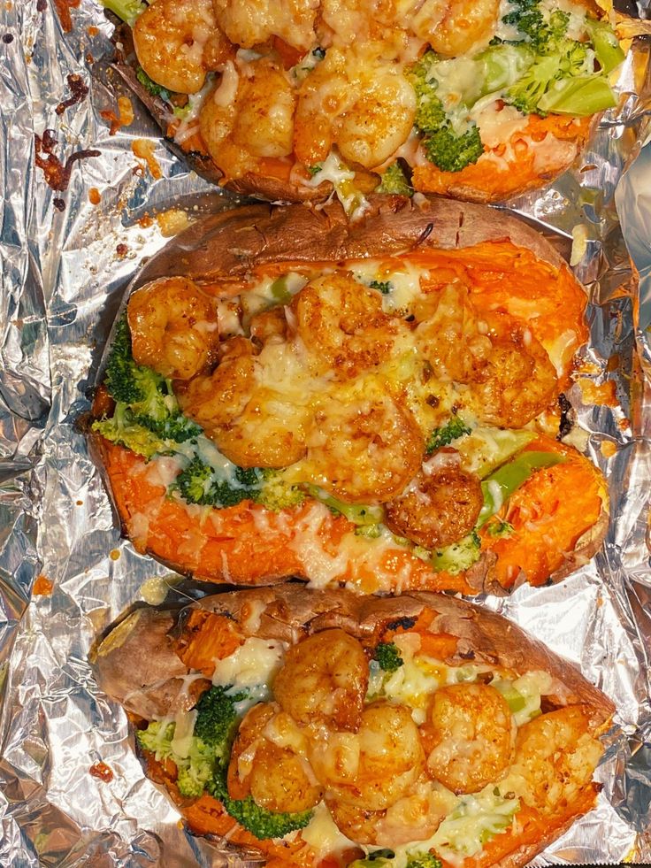 three sweet potatoes with shrimp, broccoli and cheese on them sitting on tin foil