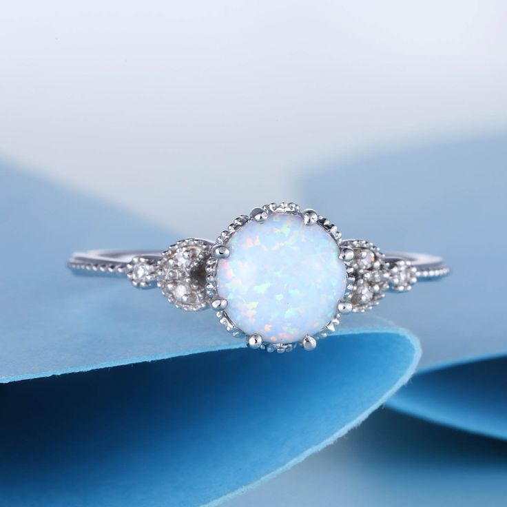 a white opal and diamond ring on top of blue paper