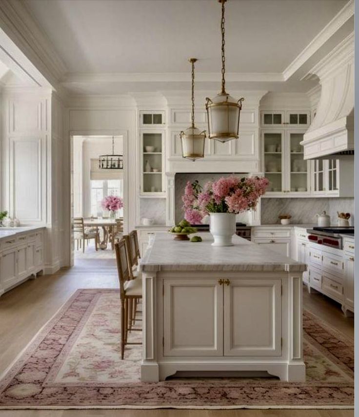 a large kitchen with white cabinets and pink flowers in vases on the center island