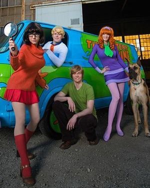 three people and a dog pose in front of a van painted with the characters of scooby