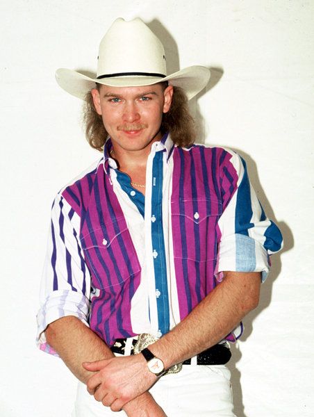 a man with long hair wearing a purple and white shirt is standing in front of a white wall