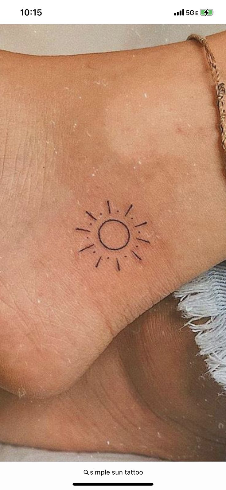 a small sun tattoo on the side of a woman's foot, with an arrow