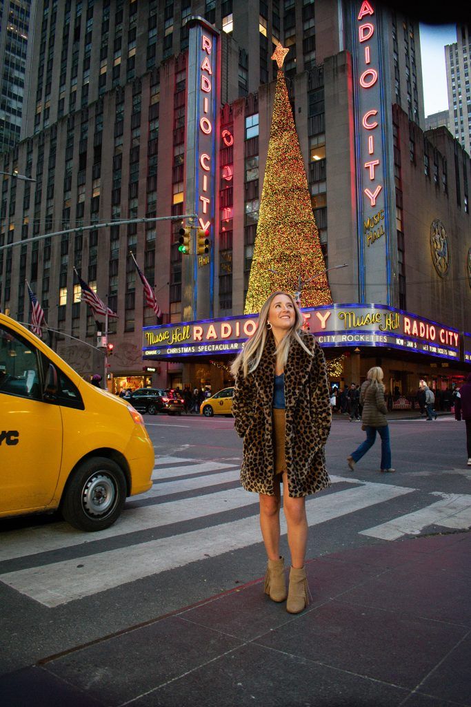 a woman standing on the street in front of a christmas tree and radio city sign