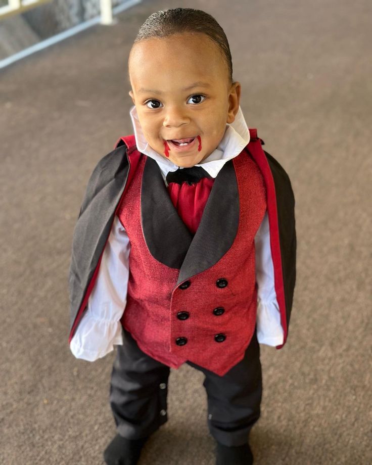 a young boy wearing a red vest and black pants with a bow tie on his head