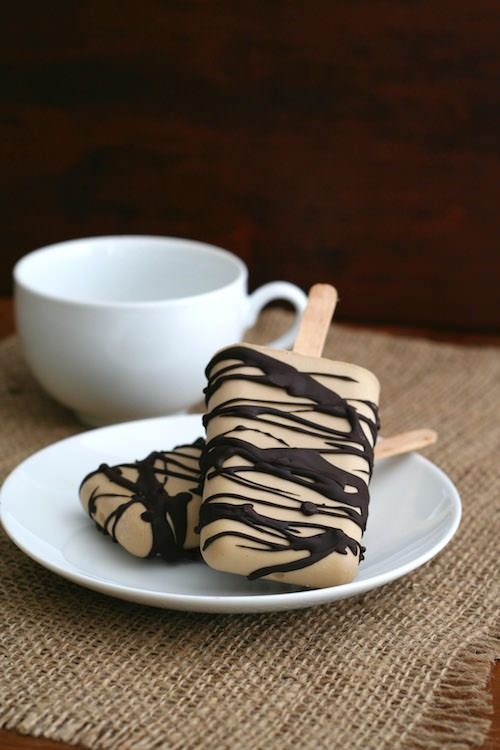 two pieces of chocolate covered ice cream sitting on top of a white plate next to a cup