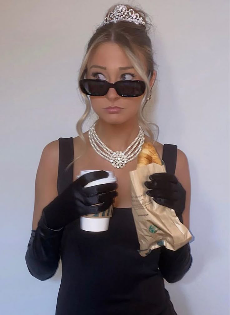 a woman wearing black gloves and holding a coffee cup in her right hand while wearing a tiara