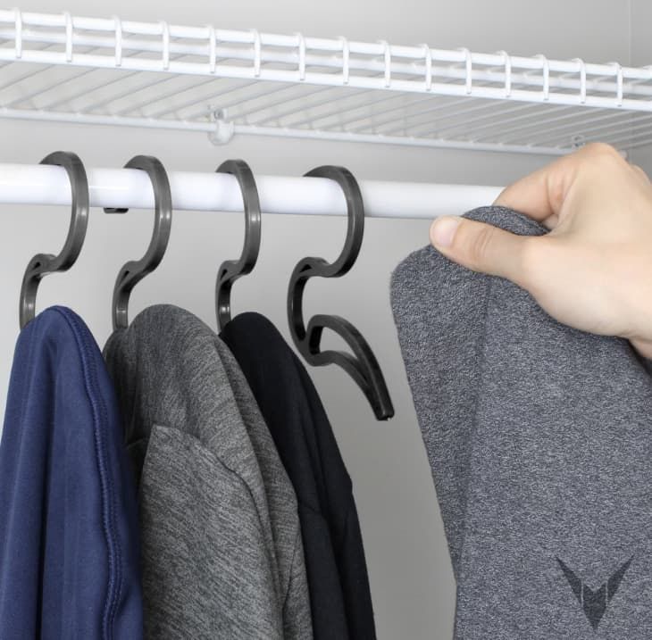 a person's hand hanging clothes from a rack on a white coat hanger