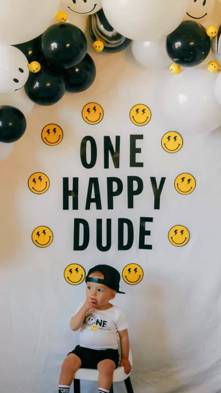 a young boy sitting on top of a chair in front of balloons with the words one happy dude