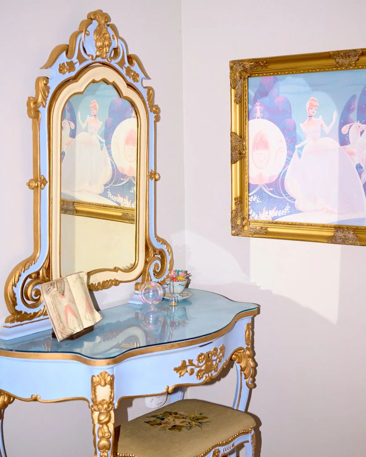 a vanity and mirror in a room with disney princess paintings on the wall behind it