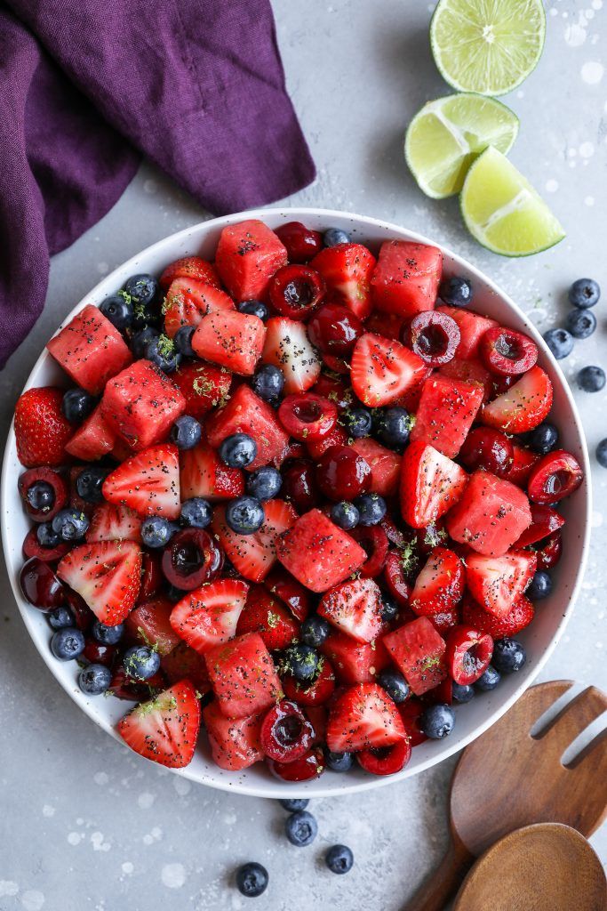 a bowl filled with berries and blueberries next to lime wedges on a table