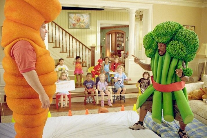 a man in an orange carrot costume standing next to a bunch of broccoli