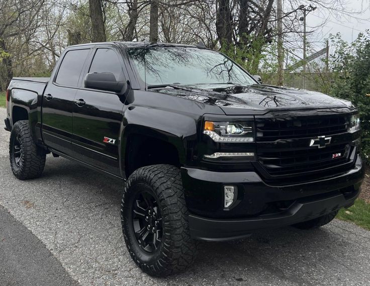 a black truck is parked on the side of the road in front of some trees