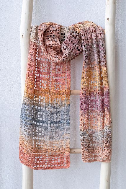 a multicolored scarf hanging on a white wall next to a wooden ladder with an object in it