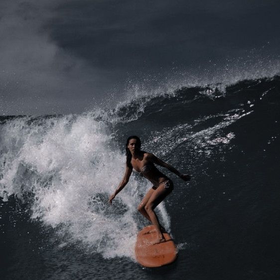 a woman riding a surfboard on top of a wave in the ocean at night