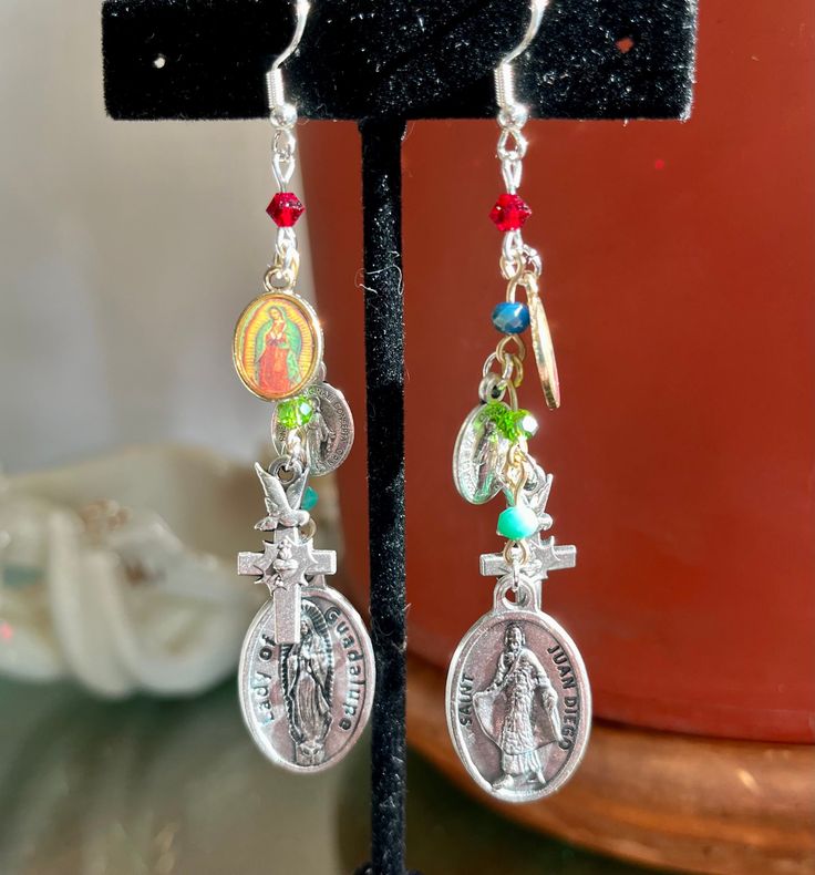 "Our Lady of Guadalupe and Juan Diego medal Earrings. Smaller colorful Guadalupe medals at the top. Then our Lady medals 'Regina Sine Labe Originali Concepta'.  Small Sacred Heart Dove Crosses Ending with the larger Juan Diego/Our Lady of Guadalupe double sided medals.  The medals all dangle from Colorful crystal beads that go with the theme. Red, beautiful blue/green iridescent color, green and turquoise. The earrings are 3 1/4\"s long and 1/2\" wide. I also have clip on ear findings.  All jewe Juan Diego, Iridescent Color, Catholic Medals, Our Lady Of Guadalupe, Lady Of Guadalupe, Etsy Earrings Dangle, Sacred Heart, Our Lady, Chandelier Earrings