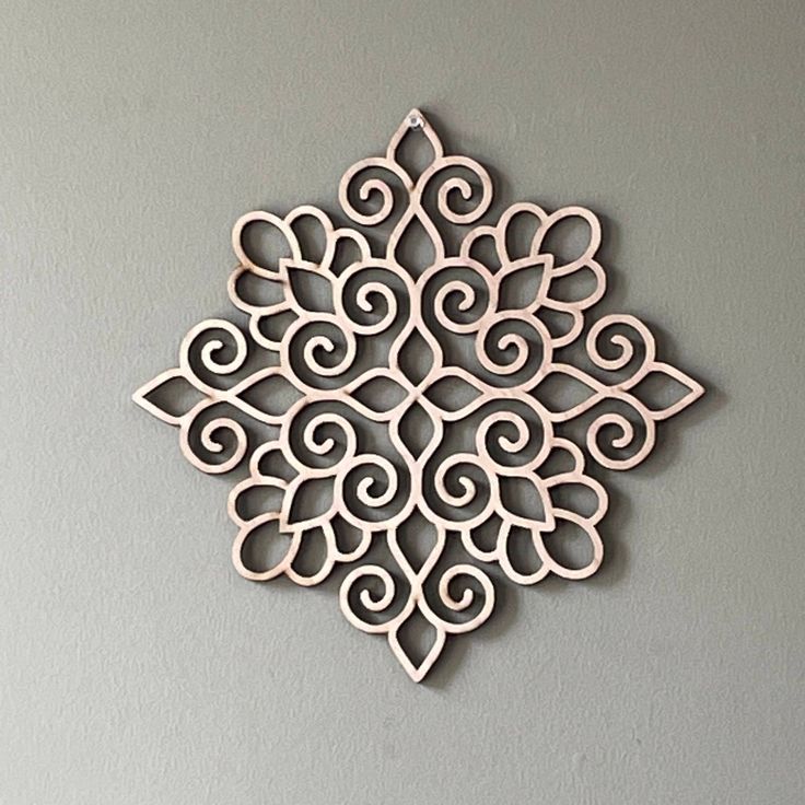 an intricate wooden ornament hanging on the wall in front of a gray wall