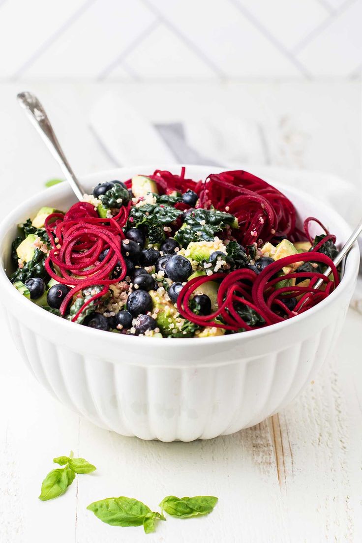 a white bowl filled with salad topped with beets and blueberries next to a spoon