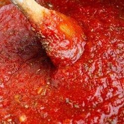 a wooden spoon stirring red sauce in a pot