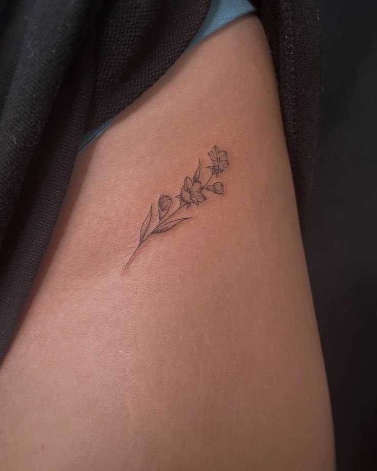 a small flower tattoo on the back of a woman's thigh, it has four petals