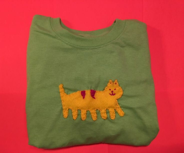 a green t - shirt with a yellow cat embroidered on it