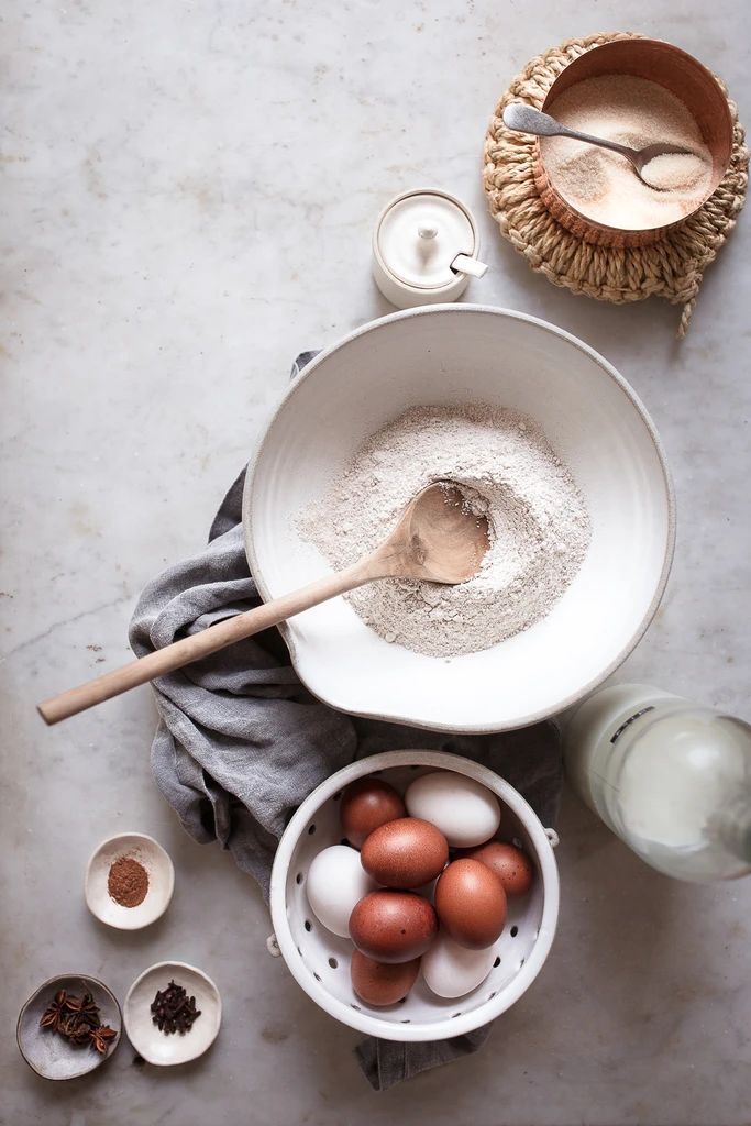 an overhead view of eggs, flour and other ingredients in bowls on a marble countertop