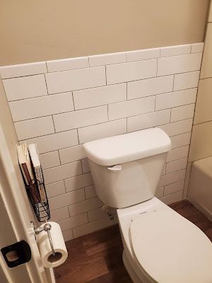 a white toilet sitting in a bathroom next to a roll of toilet paper on top of a wooden floor