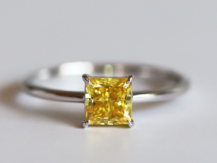 a yellow diamond ring sitting on top of a white surface with the center stone missing