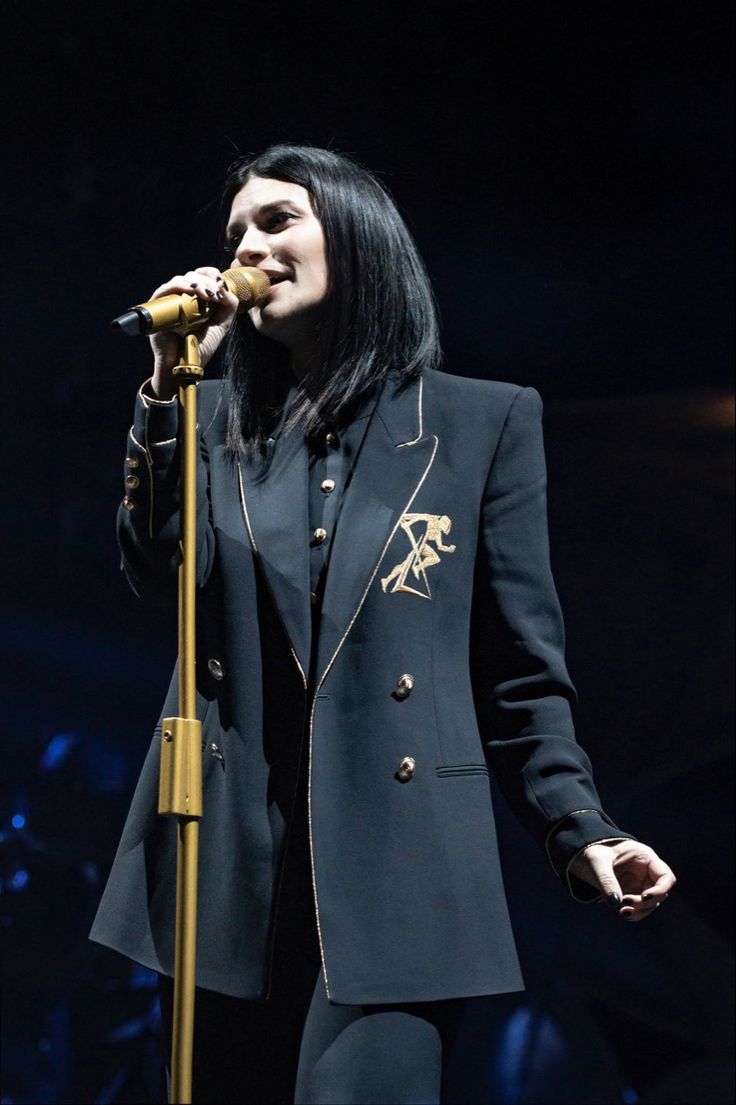 a woman with long black hair is holding a microphone in her hand and singing into the microphone