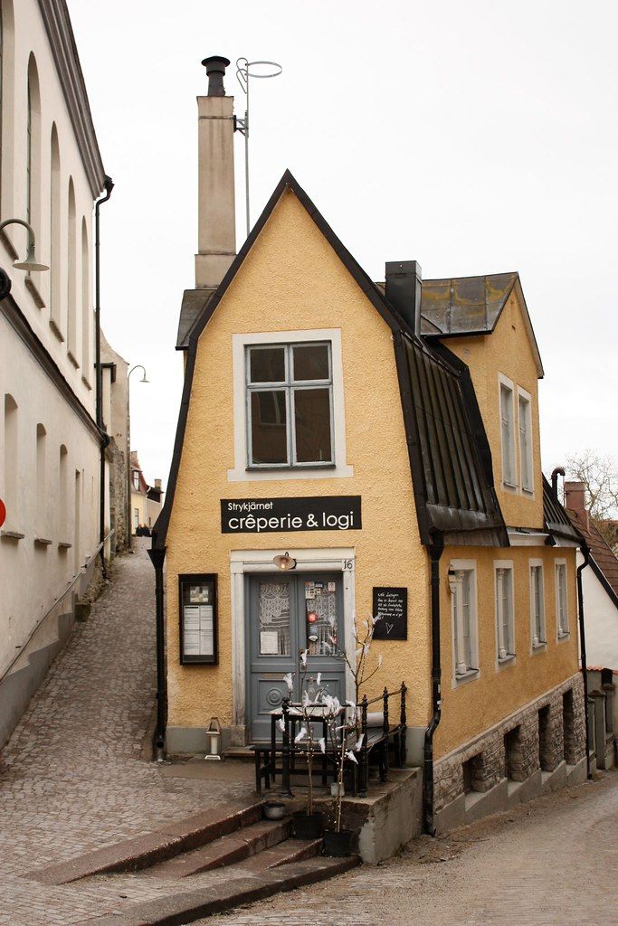 a small yellow building sitting on the side of a cobblestone road next to tall buildings