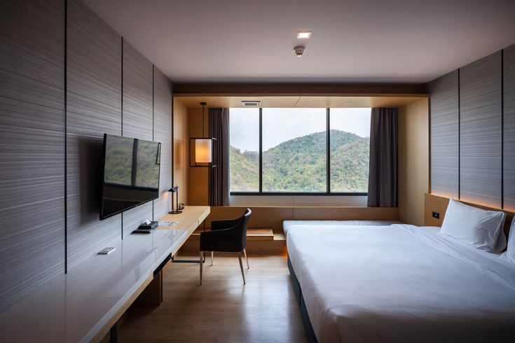 a hotel room with a bed, desk and television in the corner near a window