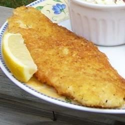 a fish fillet on a plate with a side of coleslaw and lemon wedges