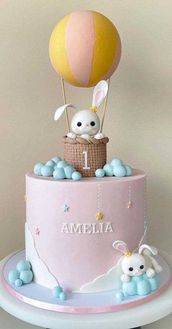 a pink cake with two bunnies and an air balloon on top that reads 1