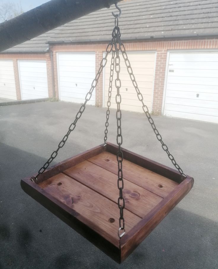 a wooden swing with chains hanging from it's sides in front of a garage