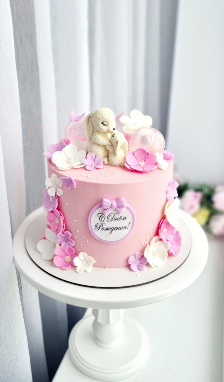 a pink cake decorated with flowers and a teddy bear