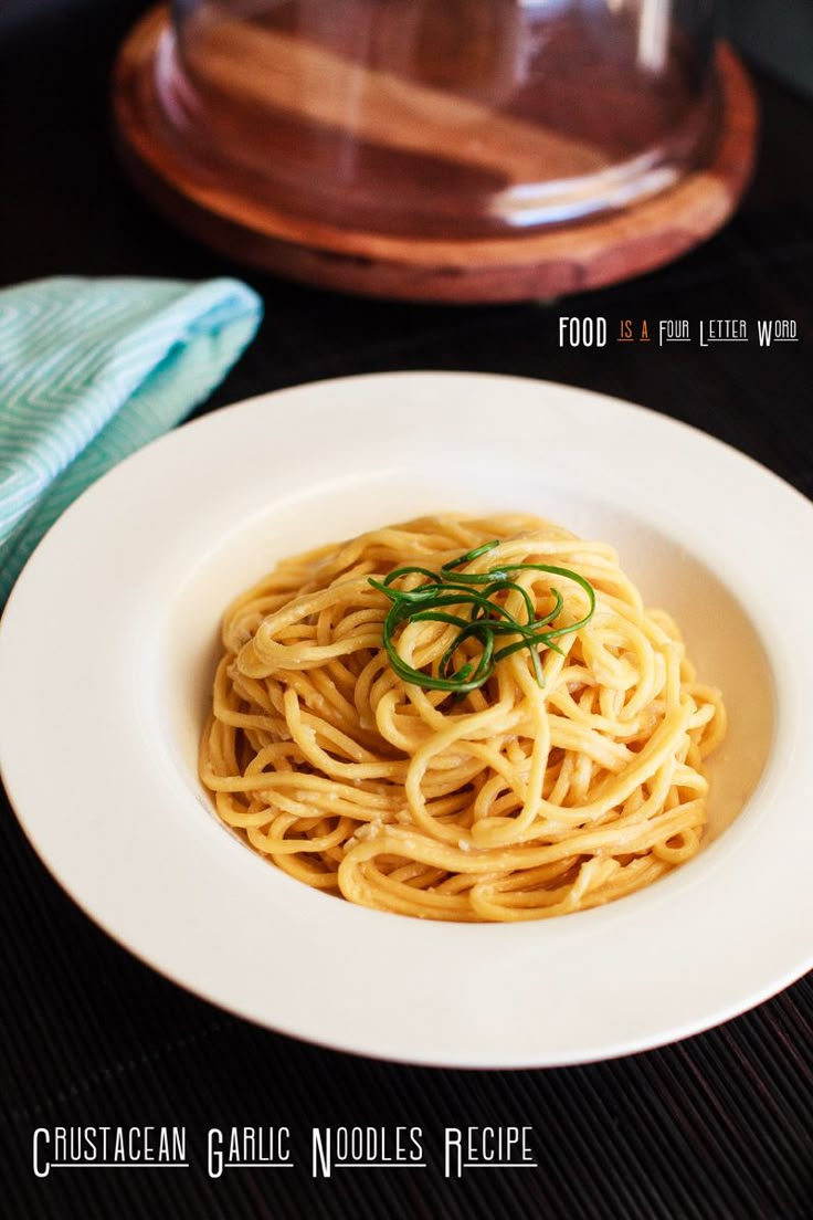 a white plate topped with pasta on top of a wooden table next to a glass container