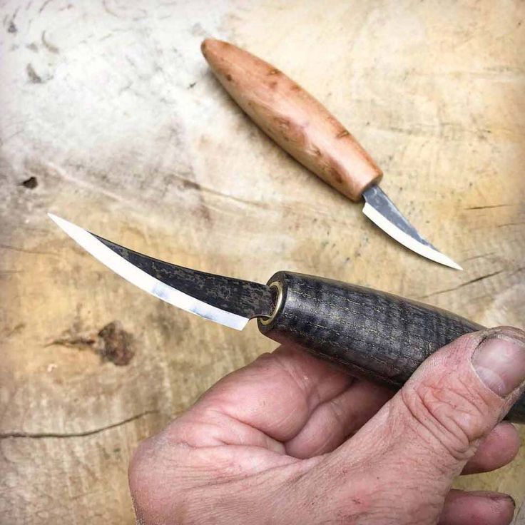 a person holding a knife in their hand next to a wooden board with two knives on it