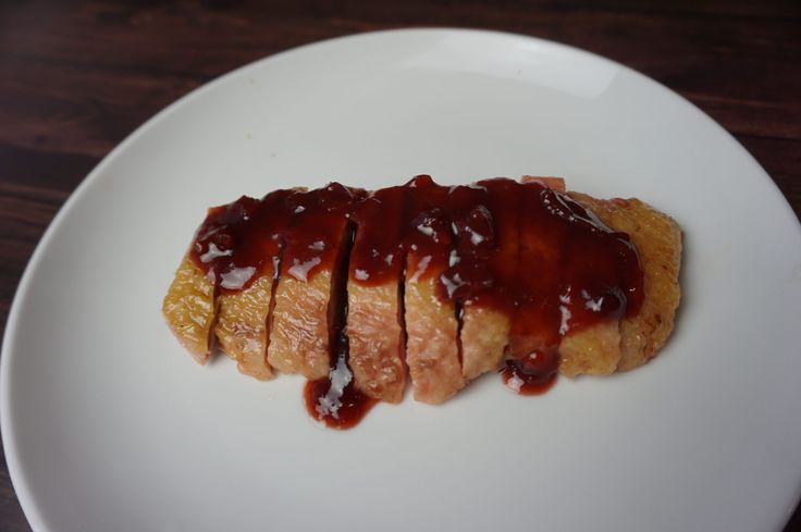 a white plate topped with meat covered in ketchup on top of a wooden table