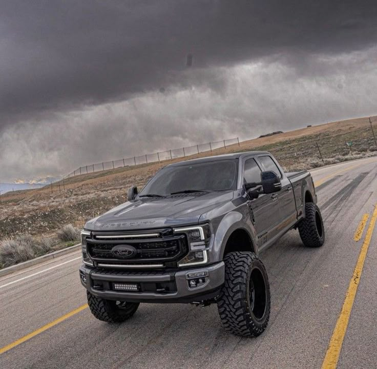 a silver truck driving down the road under a dark sky with clouds in the background