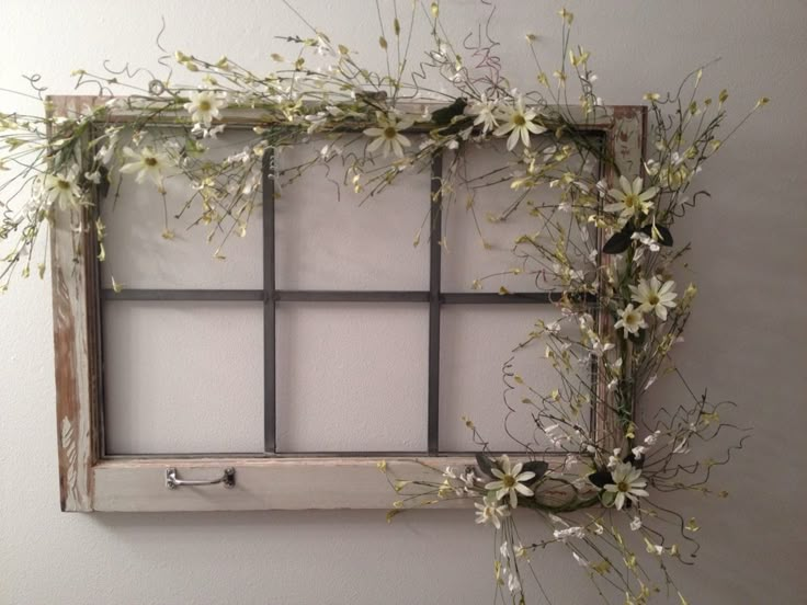 an old window frame with flowers hanging on the side and some branches in front of it