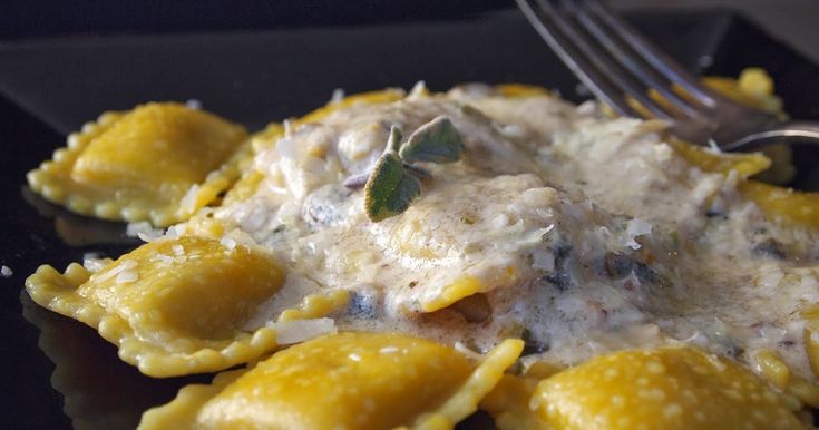 a black plate topped with ravioli covered in cheese sauce and a fork next to it