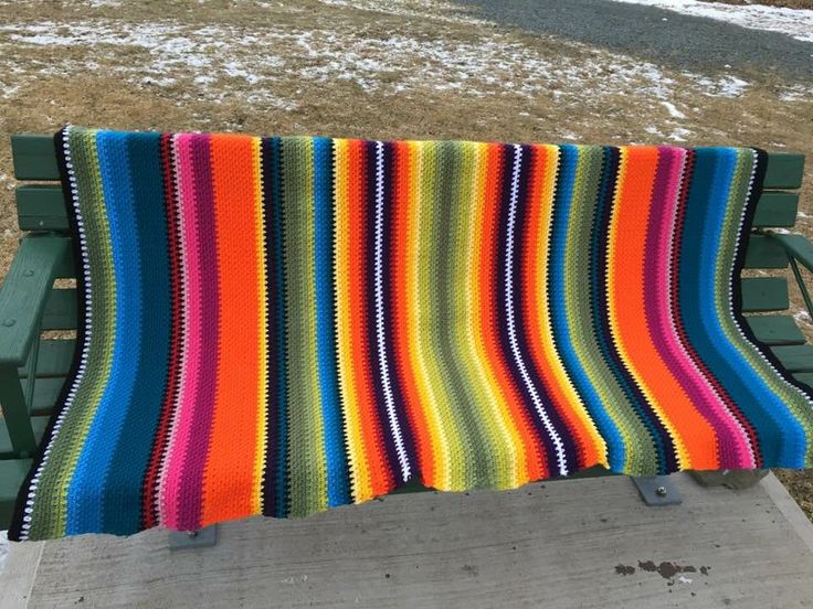 a multicolored blanket sitting on top of a green bench next to snow covered ground