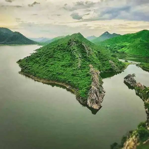 an island in the middle of water surrounded by green hills and trees on both sides