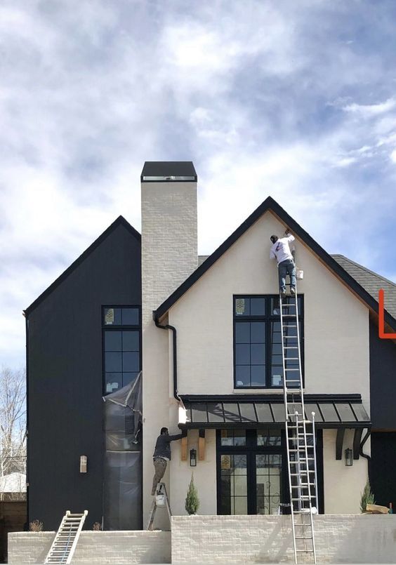 a man standing on a ladder in front of a house that is painted black and white