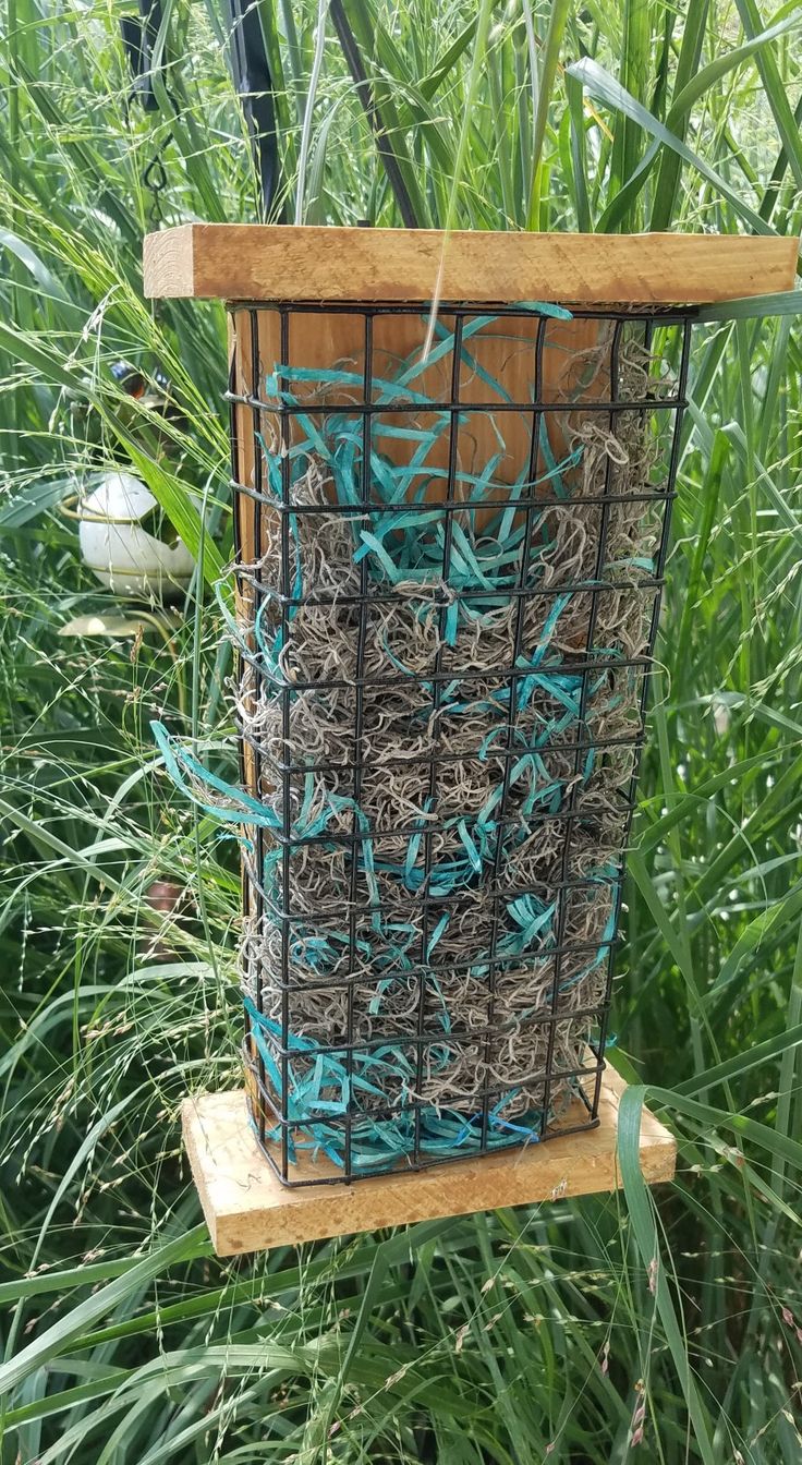 a bird feeder made out of wire and wood in the middle of some tall grass