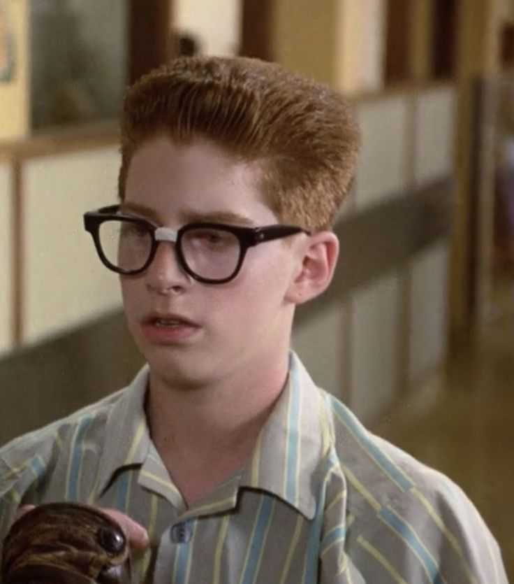 a young man wearing glasses and holding a glove in his hand while standing next to another person