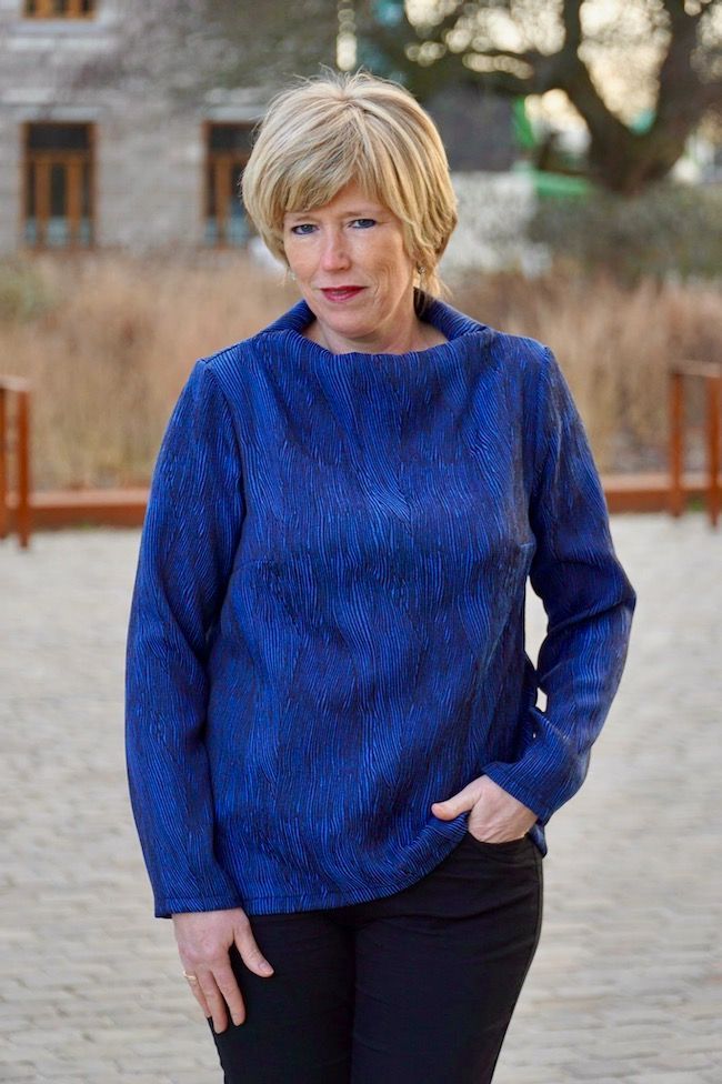 a woman standing in front of a building wearing a blue shirt and black pants with her hands on her hips