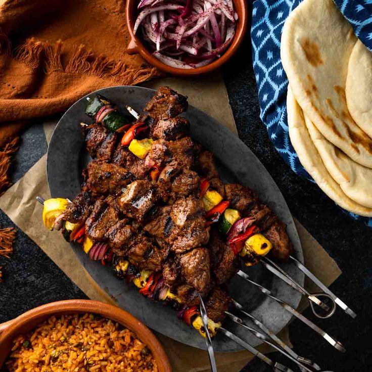 a plate with meat and vegetables on it next to some pita bread, rice and other foods